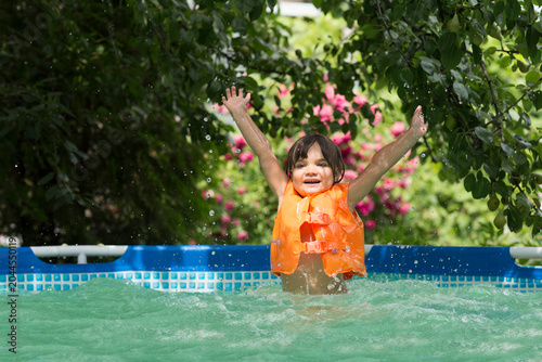 Happy child playing in the pool in the garden on a hot summer day. Summer time concept background.