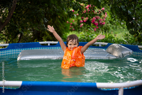 Happy child playing in the pool in the garden on a hot summer day. Summer time concept background.