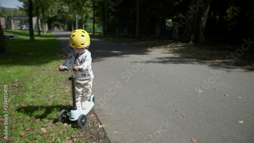 Εκτύπωση καμβά Toddler riding scooter on park path wearing yellow helmet, slows down and stops