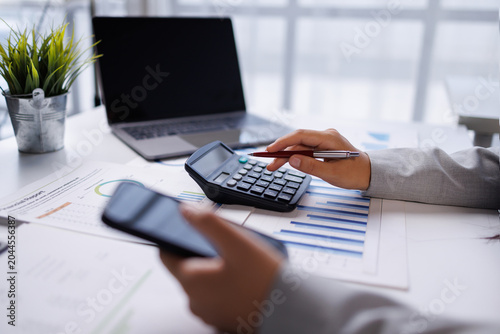 Professional hands busy calculating finances. Business person working with a calculator, smartphone, laptop and financial reports on a clean office desk, managing budget and investment planning