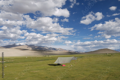 Photos A camping tarp shelter pitched on a vast green alpine meadow against majestic desert mountain ranges under a beautiful cloudy blue sky in Ladakh, Himalayas