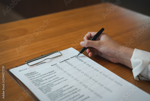 Person filling mental health checklist on clipboard with pen, psychological assessment, self evaluation, healthcare screening and wellbeing awareness concept.