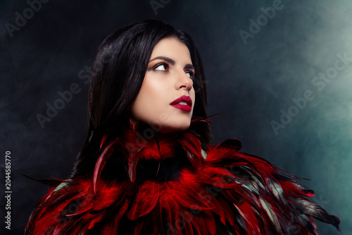 Young woman in feathered costume posing in moody lighting, representing sophistication and mysterious glamour