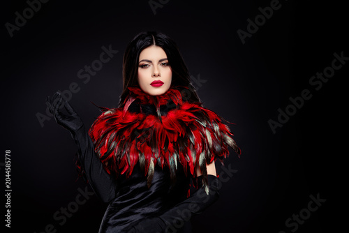 Elegant brunette woman in a luxurious red feather collar and black dress on a dark mysterious background