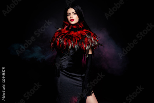 Brunette woman in dramatic black dress with feathered collar on dark smoky background