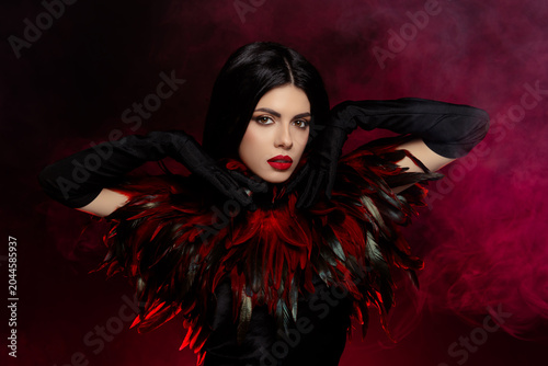 Elegant young woman dressed in a luxurious feathered costume with dramatic lighting and a smoky background