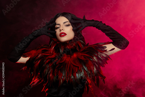 Attractive young woman in a luxurious feather costume posing confidently in a smoky atmosphere