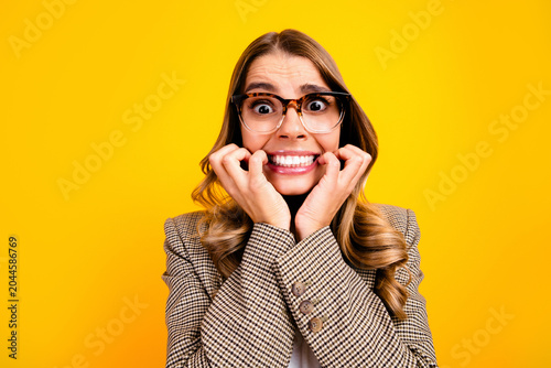 Cuadro en lienzo Nervous young woman in glasses biting her nails and smiling awkwardly against a