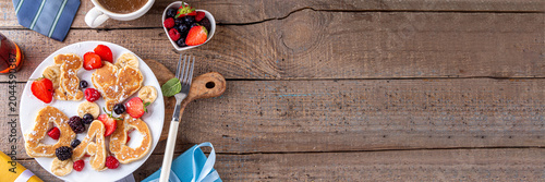 Father's day celebration with tasty pancakes in form of text i love dad and heart, with fresh berry, hot coffee or tea cup, maple sirup, newspaper, tie, glasses and gift box on cozy wooden background