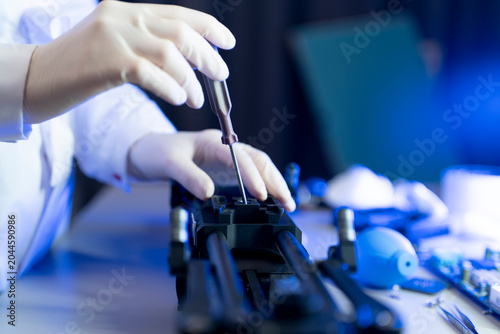 A person works on fixing a device with a screwdriver in a workshop filled with tools and equipment