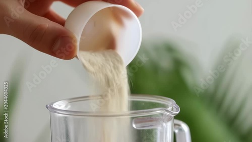Adding protein powder to a blender for a nutritious shake. Preparing healthy meals for fitness and wellness