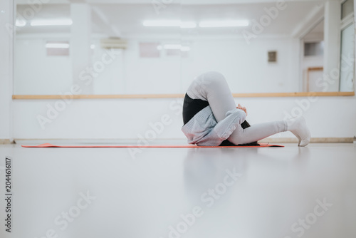 Tableau sur toile A dancer in a bright studio performs an intense forward fold stretch while curled on a red mat