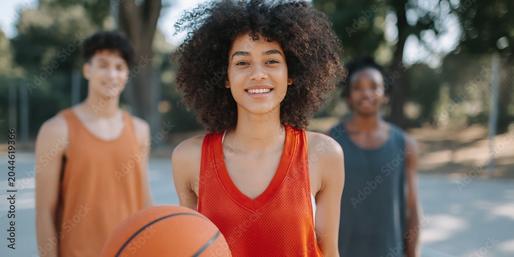 Naklejka premium Teen girl posing with basketball alongside teammates on court