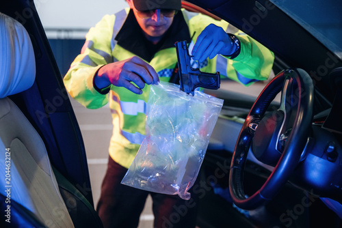 Φωτογραφία Police officer in reflective jacket examines evidence bag containing firearm ins