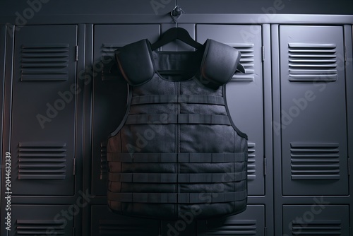 Tactical vest with padded shoulders hangs in a dark locker room