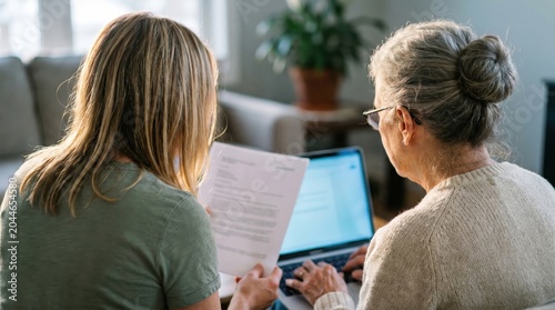 Young woman and senior reviewing documents at laptop home care assistance