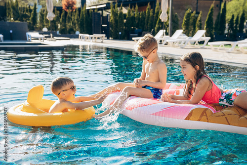Obraz na plátně Three happy children splashing and playing in a sunny resort pool during a joyfu