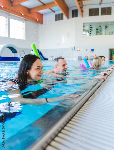 Smiling woman and group of people relaxing at the edge of an indoor swimming pool during an aqua aerobics class