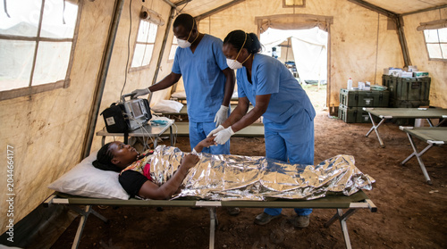 Medical professionals attend to a patient in a tent clinic during a health crisis