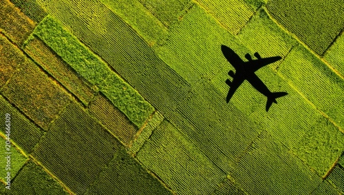 Silhouetted aircraft soars over geometric patterns of lush green fields