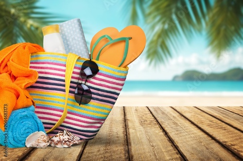 Sticker Striped beach bag with summer accessories on a wooden table with tropical sea ba