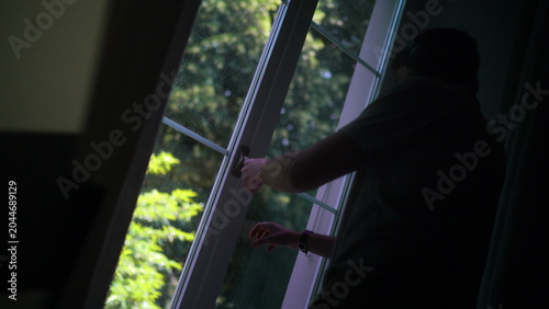 Принти на полотні Man opening window while wearing headphones and briefly looking outside at trees