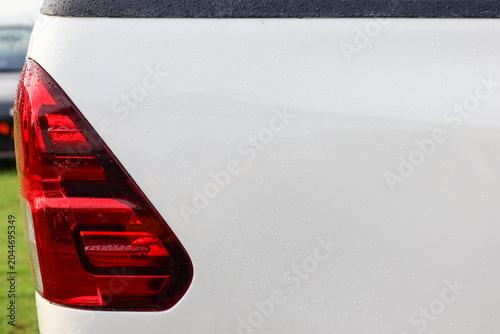 Close-up view of a red rear taillight assembly on a white pickup truck body covered in fresh rain water droplets.
