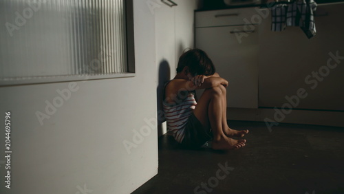 Fotografía Lonely child sitting on kitchen floor with head down in corner expressing sadnes