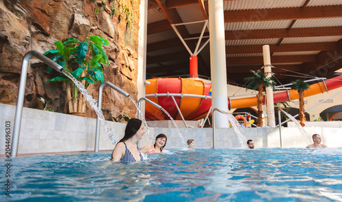 Happy mature woman relaxing with friends under a water fountain in an indoor swimming pool at a water park