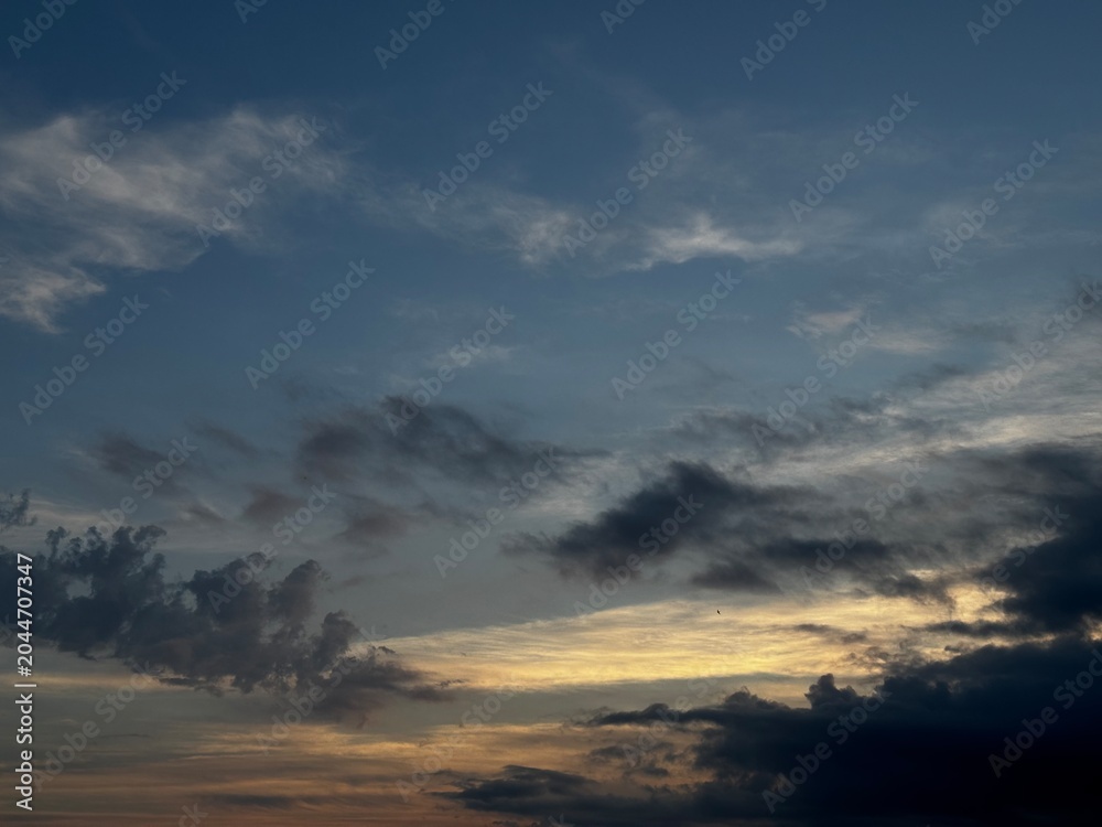 Fototapeta premium Dramatic evening sky with dark clouds and soft golden sunset light. Atmospheric cloudscape background with moody weather, natural twilight colors and spacious copy space.