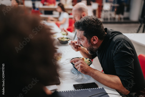 Obraz na plátně A businessman eats lunch from a bowl while seated at a communal office table