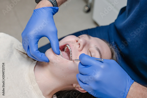 Obraz na plátne Dental professional in blue gloves inspecting metal braces using angled mirror and probe on teen patient reclined in chair