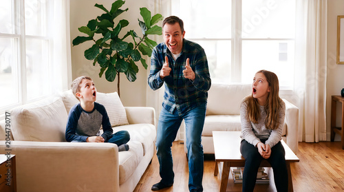 Father making funny dad jokes gestures with children in living room