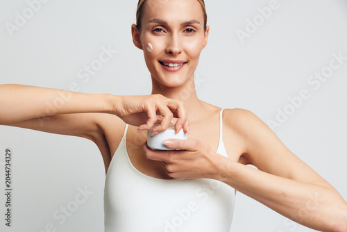 Quadro su tela Smiling woman applying white face cream on her cheek