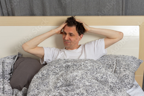 Fotografie A 53-year-old man wakes up in his bedroom and sits up in bed