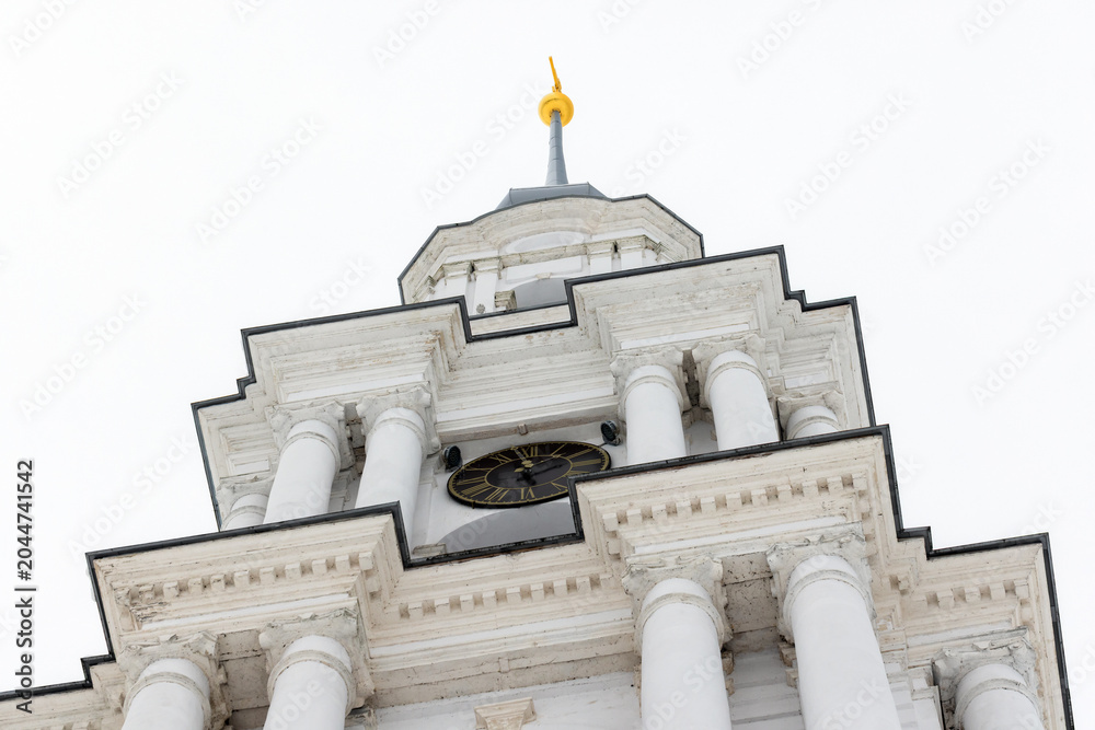 Fototapeta premium Close up photo of a tall white bell tower rises under overcast winter sky. The Flooded Belfry, Kalyazin, Tver Oblast, Russia. White neoclassical church tower built in 1796–1800