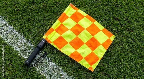 Close-up of an orange and yellow checkered referee's flag resting on green grass with a white line on a sports field
