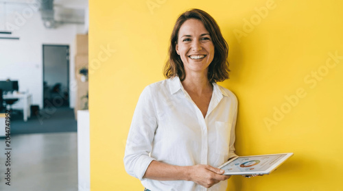 Confident Female Entrepreneur Holding Tablet with Business Infographics Against a Yellow Background