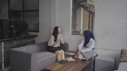 Two women sharing pastry on table while conversing one wearing headscarf offering guidance mentor and mentee dynamic casual snack
