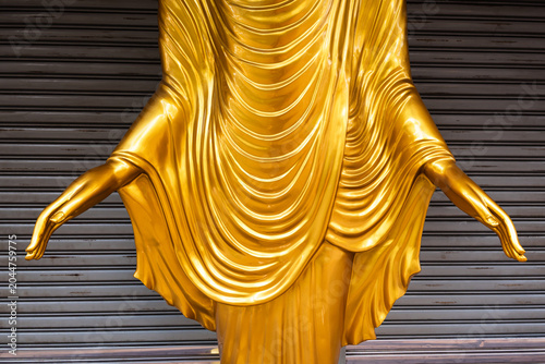 Close-up of Golden Buddha Statue Hands and Robe against Metal Shutter Background