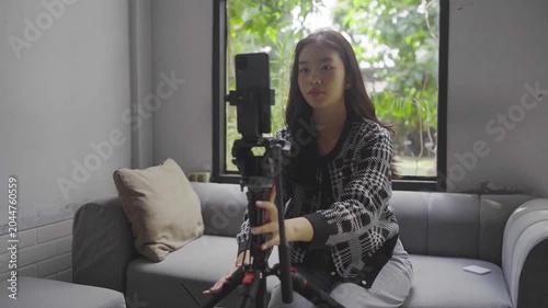 Asian woman adjusting camera tripod and lens, focused behind scenes tutorial, manual framing and focus checks, handson equipment
