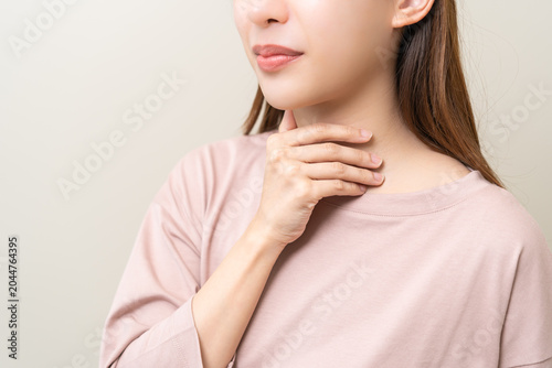 Sickness in inflaming asian young woman, girl use hand check self touch at sore throat, pain thyroid gland on neck or disease reflux, acid of suffer people on wall background. Medical and healthcare.