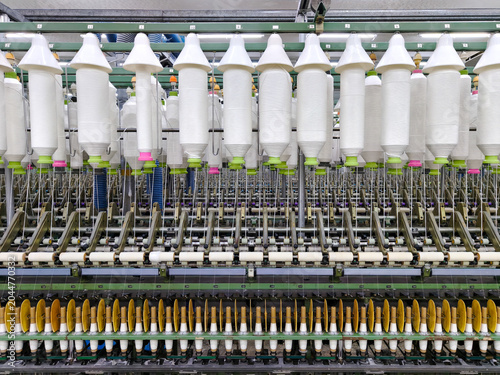 Wide angle of massive industrial spinning machine rows with white yarn cones