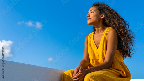 Bright sunny day where a woman in a yellow dress enjoys the peaceful moment by the sea under a clear blue sky