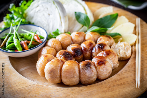 Foto Grilled Thai Isaan sour pork sausage served with fresh cabbage, chilies, and herbs on a wooden plate