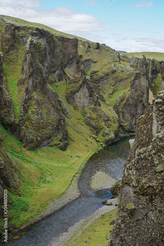 Fotografie A deep canyon with a winding river flowing through lush green valleys and rugged rock formations under a partly cloudy sky