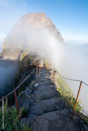 Narrow mountain trail between Pico do Arieiro and Pico Ruivo on Madeira Island, Portugal. Scenic hiking path overlooking a deep valley filled with inversion clouds and mist.