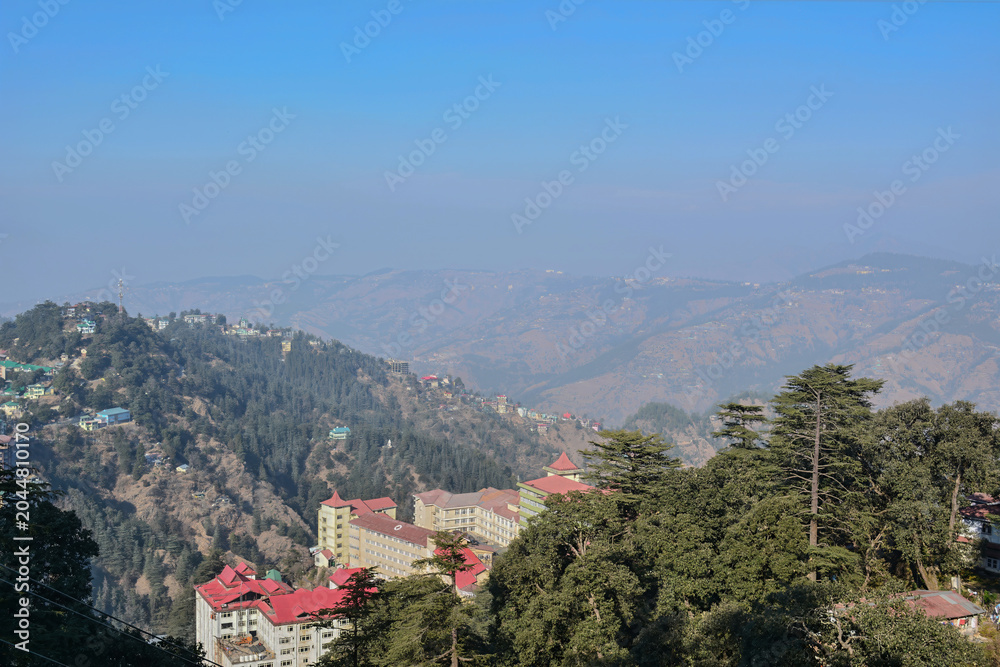 Fototapeta premium Sprawling hillside settlement with diverse rooftop styles is layered against a backdrop of hazy mountain ranges perfect for urban growth, community living, high-altitude housing, human adaptation