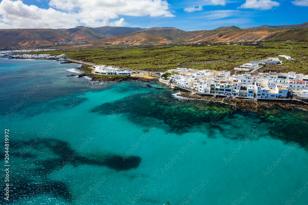 Fototapeta premium The coastline of Punta Mujeres in Lanzarote. Colorful houses line the shore while the ocean meets the volcanic hills in the background