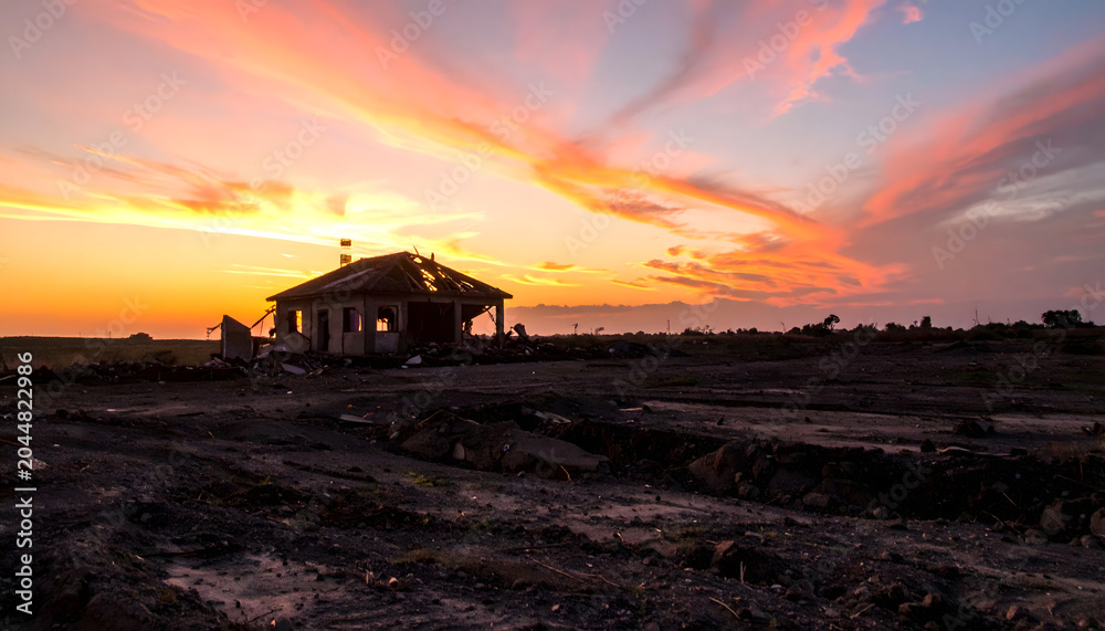Fototapeta premium Sunset over a small house in a desolate landscape with vibrant clouds